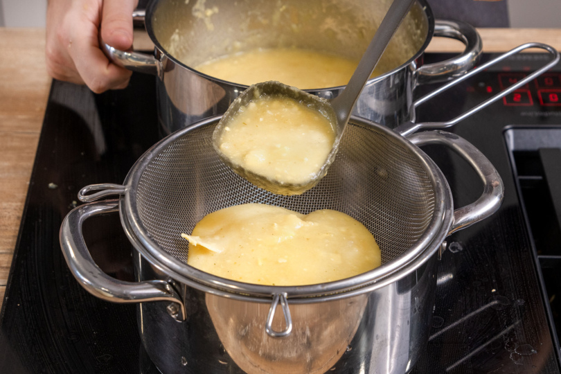 Weiße Patisson-Kürbissuppe durch ein Sieb geben